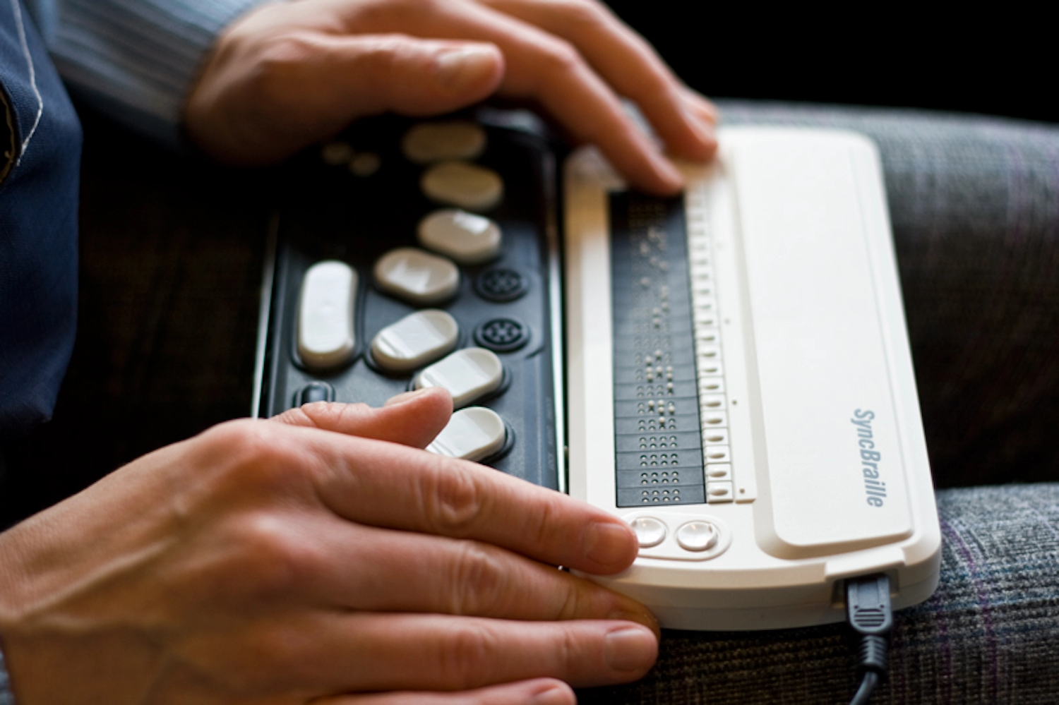 A person using a braille display running their finger over patterns of raised dots along the display.